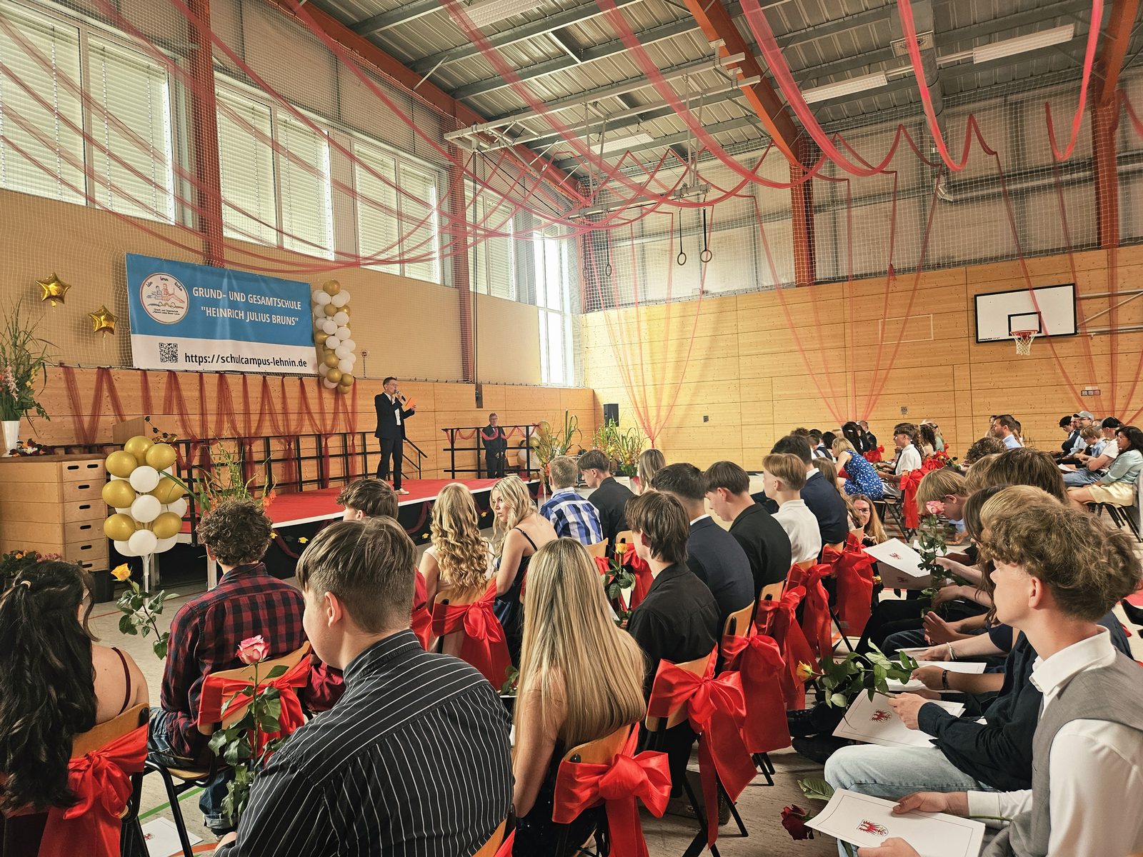 Feierliche Zeugnisausgabe der 10. Klassen in der geschmückten Sporthalle, Schülerinnen und Schüler mit Urkunden und Rosen