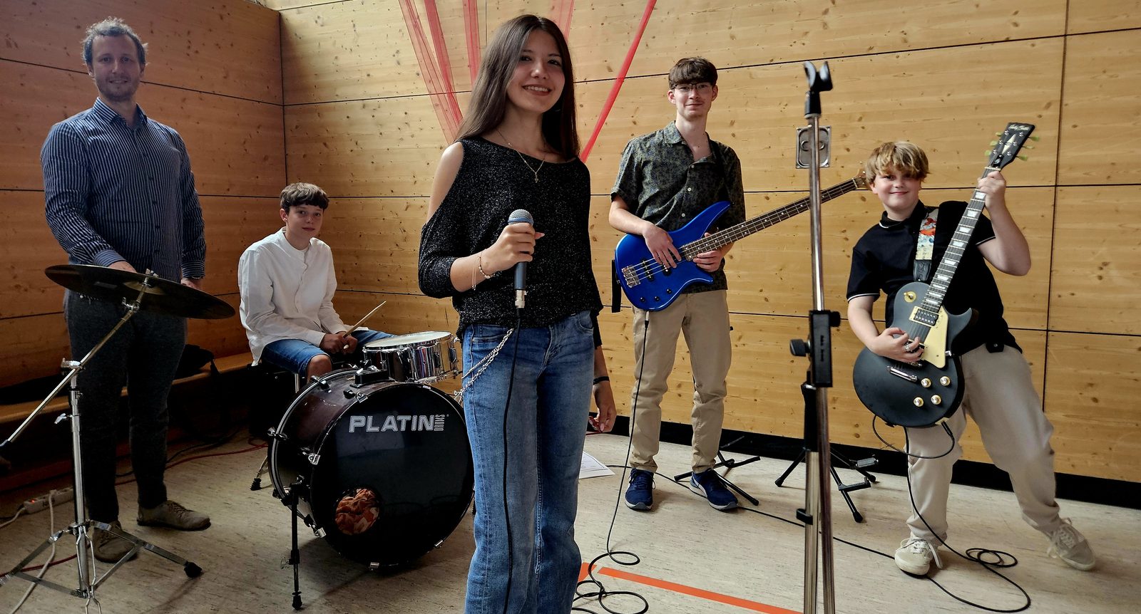 Die Schulband mit vier Jugendlichen an Gesang, Schlagzeug, Bass und Gitarre sowie ihrem Leiter